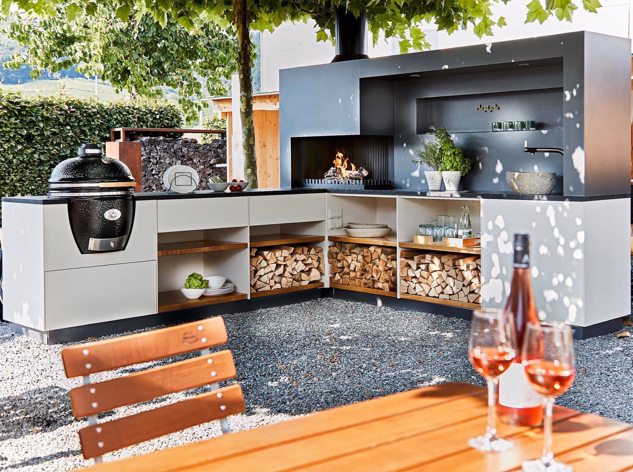 L-shaped outdoor kitchen with kamado grill, fire module and stacked firewood